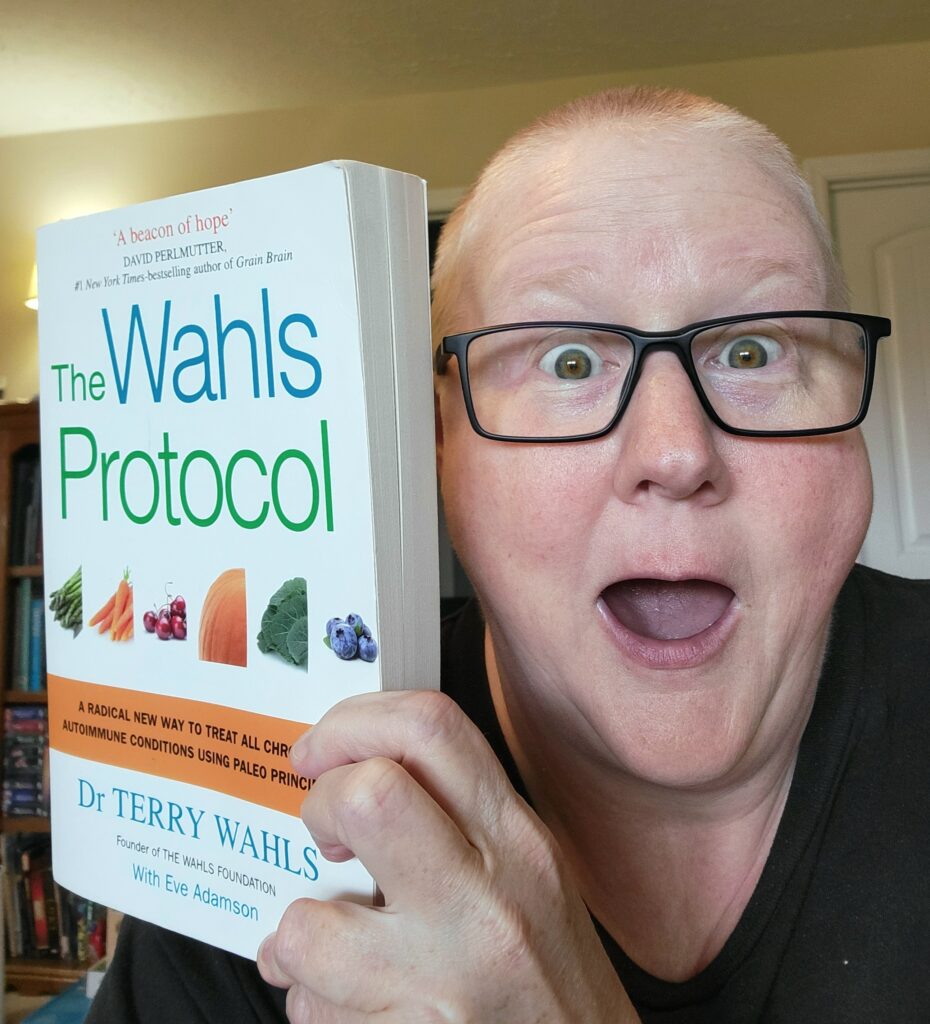 Wahls Protocol book is being held up by Janni. She has short, buzzed off hair and is wearing eyeglasses. She looks excited and amazed. 